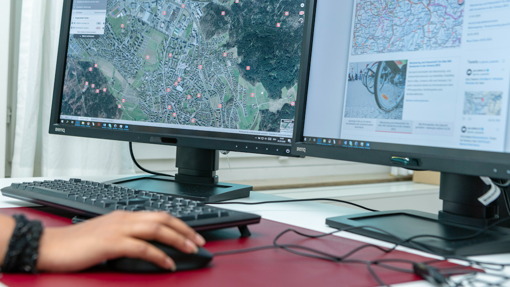 Computer-Arbeitsplatz mit Bildschirmen und Tastatur. Eine Hand hält die Maus